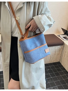 Sac seau en denim et cuir porté par un mannequin en trench-coat beige élégant
