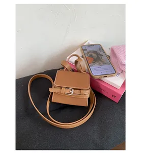 Detail of a brown leather mini crossbody bag featuring a metal buckle and slim shoulder strap