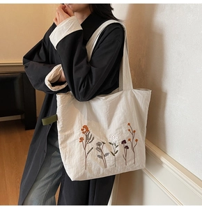 Detail of floral embroidery on a white tote bag worn by a model in a natural setting