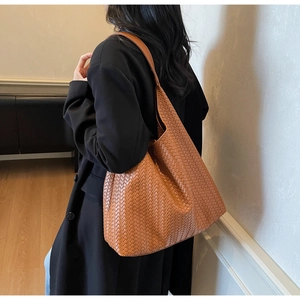 Detail of a brown woven leather tote bag shown from a stylish side angle on a model