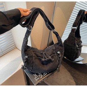 Detailed close-up of a black denim crescent bag featuring multiple zipper pockets and knotted ties