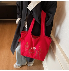 Detailed shot of vibrant red canvas tote bag with intricate floral embroidery on shoulder