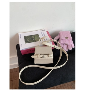Close-up of cream mini square handbag with metal buckle detail on grey knit surface