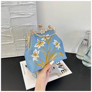 Close-up of lily floral embroidery and golden metal frame on a light blue canvas bag