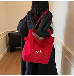 Detailed view of red canvas tote bag with floral embroidery worn by a model