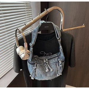 Detail of blue denim shoulder bag showing multiple zipper pockets and woven rope pulls