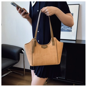 Detail of khaki woven tote bag showing dark brown leather trim and metal logo