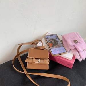 Chic tan mini crossbody bag with a buckle strap shown in a modern lifestyle setting