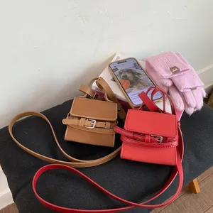 Detailed shot of mini square crossbody bags in tan and red with buckle and thin straps