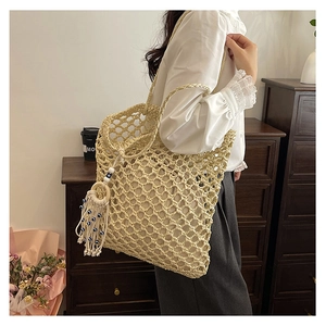 Detail of hollow woven tote bag with evil eye tassel charm and large mesh pattern