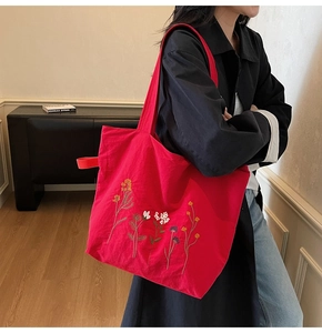 Detail of red canvas tote bag featuring vibrant floral embroidery and a wide shoulder strap