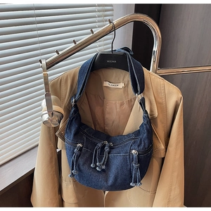 Detail of blue denim hobo bag with multiple zippers and tassels hanging on a rack