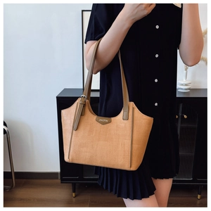 Detail of khaki woven tote bag with brown leather straps and metal logo on navy dress