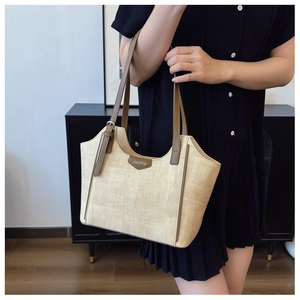 Close-up of woven straw tote bag featuring brown leather trim and handles on a model