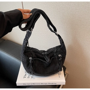Detail of black washed denim crossbody bag featuring multi-zippered pockets and rugged texture