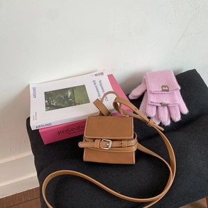 Detail shot of mini brown crossbody bag with flap closure and buckle strap on textured surface