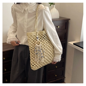 Close-up of beige woven tote bag featuring evil eye bead tassel and mesh design