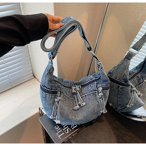Detail of blue denim crescent bag with multiple zippers and stylish rope fringe pullers
