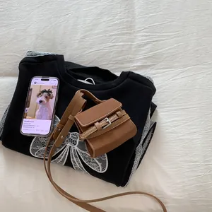 Flat lay of a brown PU leather mini flap bag with dual buckles and a lace bow sweatshirt