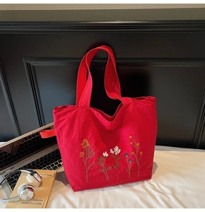 Detail view of a red canvas tote bag with floral embroidery on a white surface