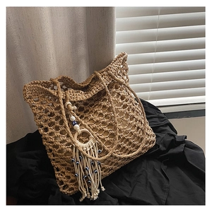 Detail of hollow woven straw tote bag featuring blue evil eye tassel and fringe charm