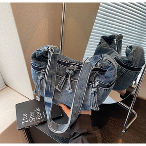Detail of blue denim crossbody bag with multiple zippers, tassels, and adjustable strap