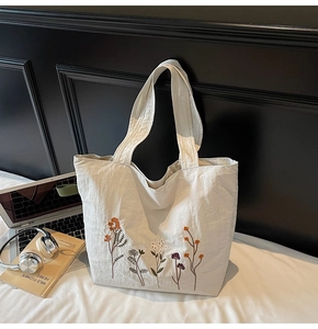 Close-up of wildflower embroidery on a beige nylon tote bag with laptop and books