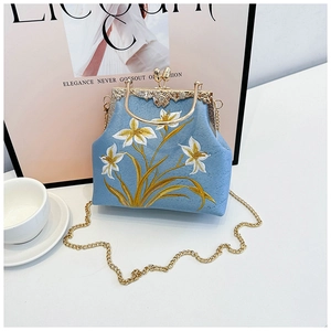 Detailed embroidery of white lilies and golden leaves on a light blue silk handbag