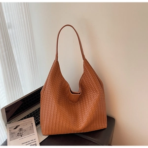 Detail of tan woven leather tote bag texture placed next to a silver laptop