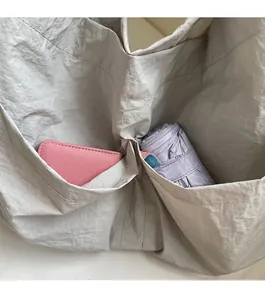 Detail shot of light grey nylon tote bag showing front pockets for storage