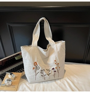 Detailed embroidery of colorful wild flowers on a white canvas tote bag with props