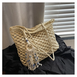 Detailed macro of beige crochet tote bag showing hollow honeycomb weave and evil eye tassel