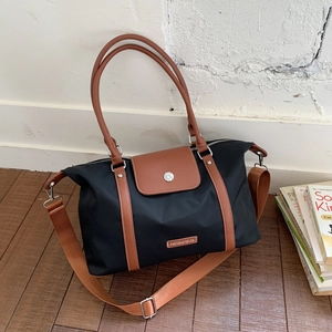 Detail of black nylon travel tote featuring brown leather handles and brand plaque