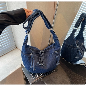 Detail view of denim crescent bag featuring multiple pockets and metal zipper tassels