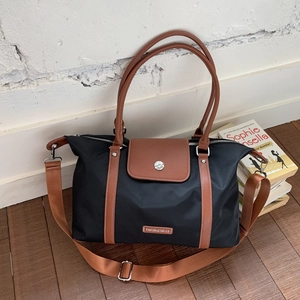 Close-up of black nylon travel tote bag with brown leather straps and metal brand plate