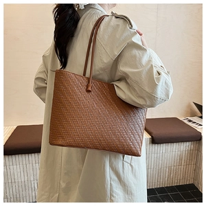 Detailed view of brown woven tote bag with slim leather handles in a minimal setting