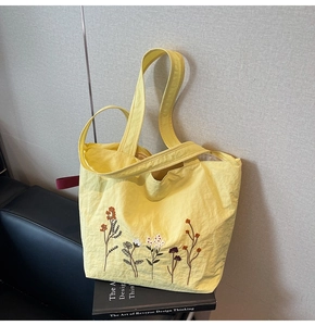 Detail of floral embroidery on yellow canvas tote bag against a minimalist background
