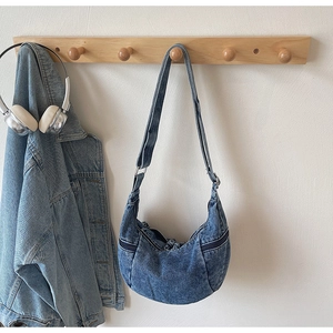 Detail of blue wash denim crescent crossbody bag with side zippers and wide shoulder strap