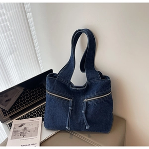 Close-up of deep blue denim tote bag featuring dual metal zippers and wide shoulder straps