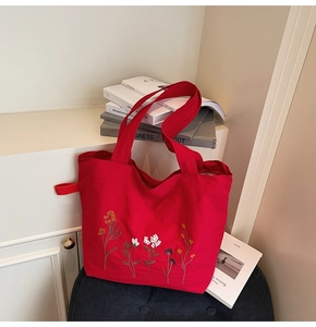 Detailed close-up of colorful floral embroidery on a vibrant red canvas tote bag fabric
