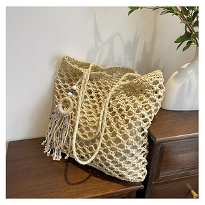 Detail of hand-woven straw tote with hollow mesh pattern and boho tassel charm