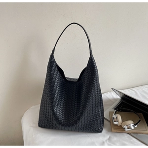 Detail of black woven hobo tote bag with smooth leather strap next to laptop