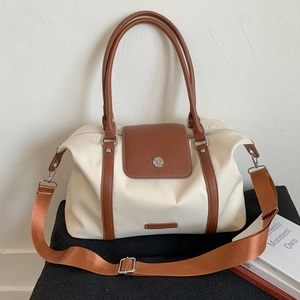 Detail of cream travel bag with brown leather trim, metal magnetic buckle and shoulder strap