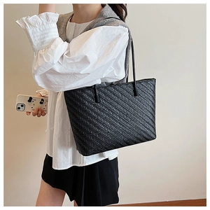 Detail of black woven leather tote bag showing intricate braided texture and slim straps