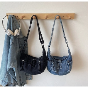 Detail view of denim crescent bags with zipper pockets and adjustable straps in blue and black