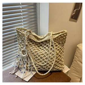 Close-up of woven hollow tote bag with evil eye tassel charm on a wooden table