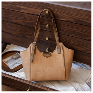 Detail of camel tote bag with woven texture, leather brand tag and silver buckle strap