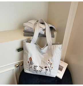 Close-up of floral embroidery on light grey canvas tote bag with textured fabric detail