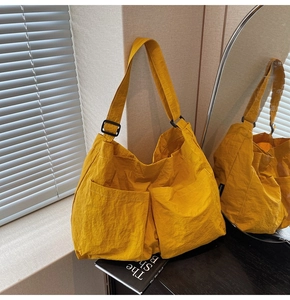 Detail of ginger yellow nylon shoulder bag featuring dual front pockets and adjustable strap