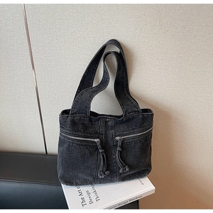 Detail of black denim tote bag with cargo zipper pockets and tassel pullers on white books